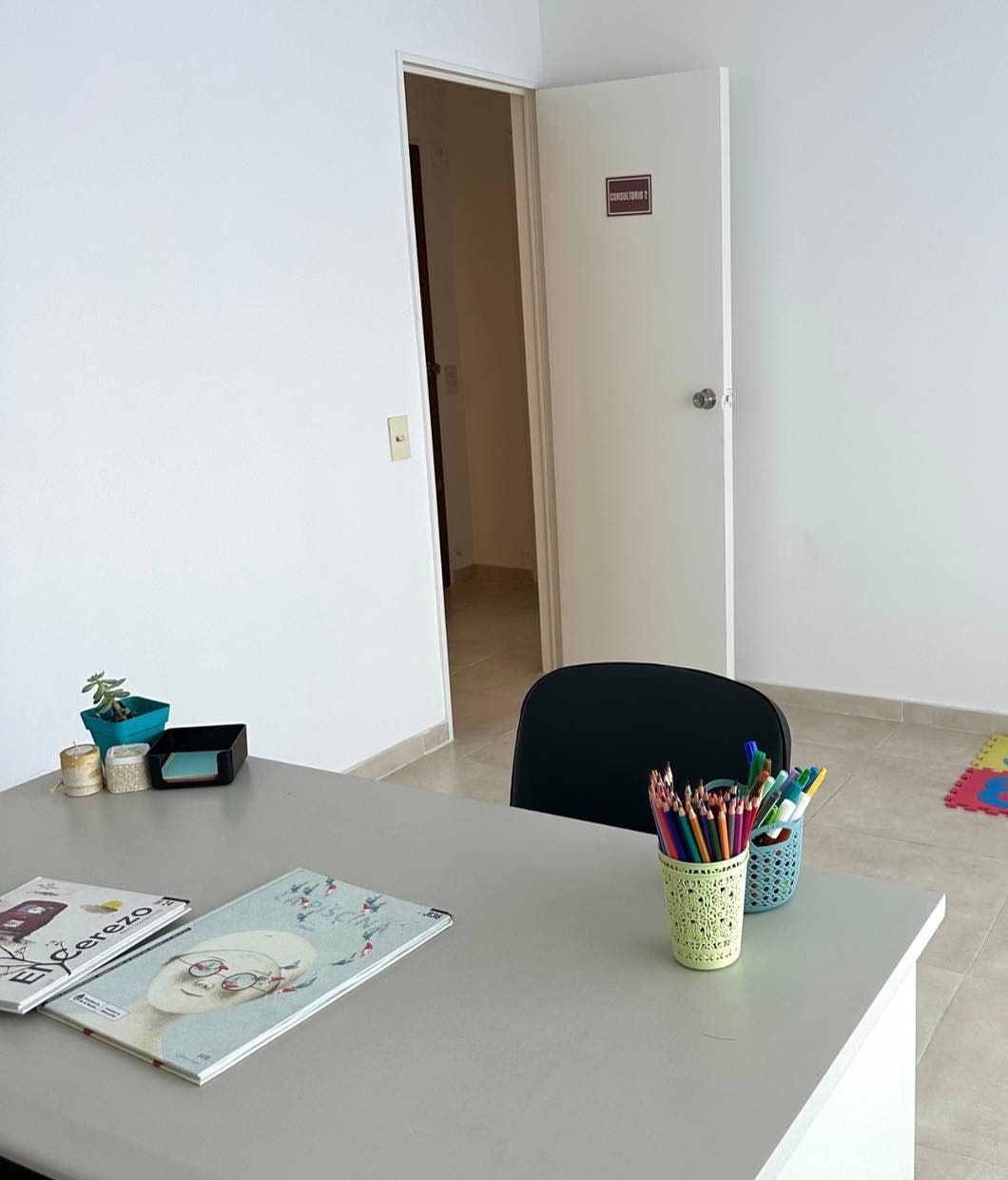 Consultorio con escritorio, lápices de colores, libros infantiles y alfombra de números junto a la puerta